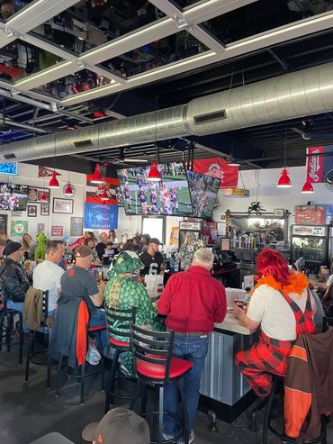 People watch a football game at a lively bar, some in costumes.