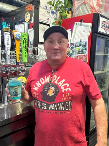 Man in red shirt holding a blue drink with a lemon slice at a bar.