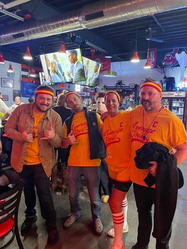 Group in matching Average Joes outfits at a bar, smiling and posing.