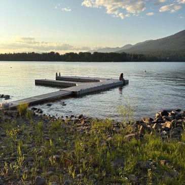 Person sitting on a dock at sunset by a lake.
