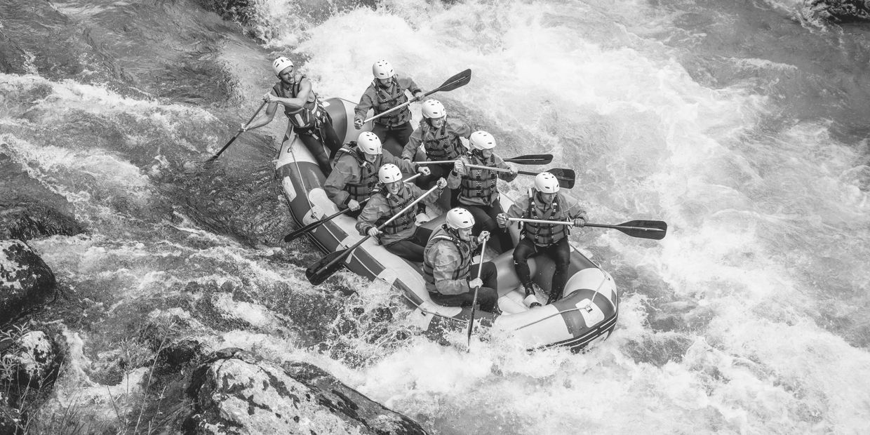 Eight people white-water rafting on a turbulent river wearing helmets and life jackets.