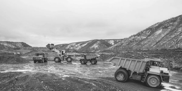 Heavy machinery including dump trucks and a loader working at a muddy mining site.