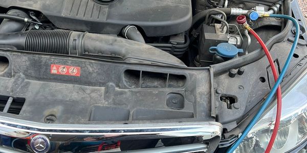 Car engine bay with charging cables connected for air conditioning service.