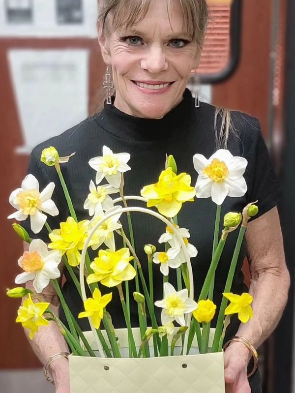 A smiling woman holding a basket of yellow and white daffodils.
