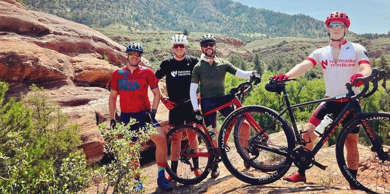 Four cyclists posing with their bikes in a mountainous landscape under a clear sky.