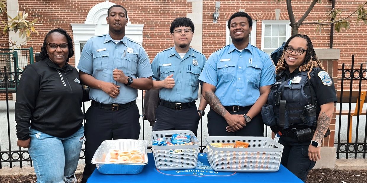 Group of officers and a woman posing behind a table with snacks.