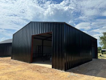 New black metal storage building with open door on dirt ground.