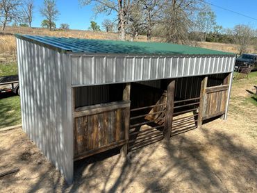 Metal and wood livestock shelter with two fenced stalls outdoors.