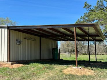 Metal shed with an attached covered area on a grassy field under a clear blue sky.