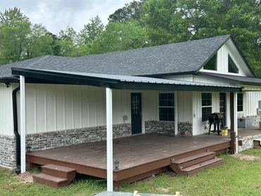 A spacious wooden porch with an overhang attached to a modern house surrounded by greenery.