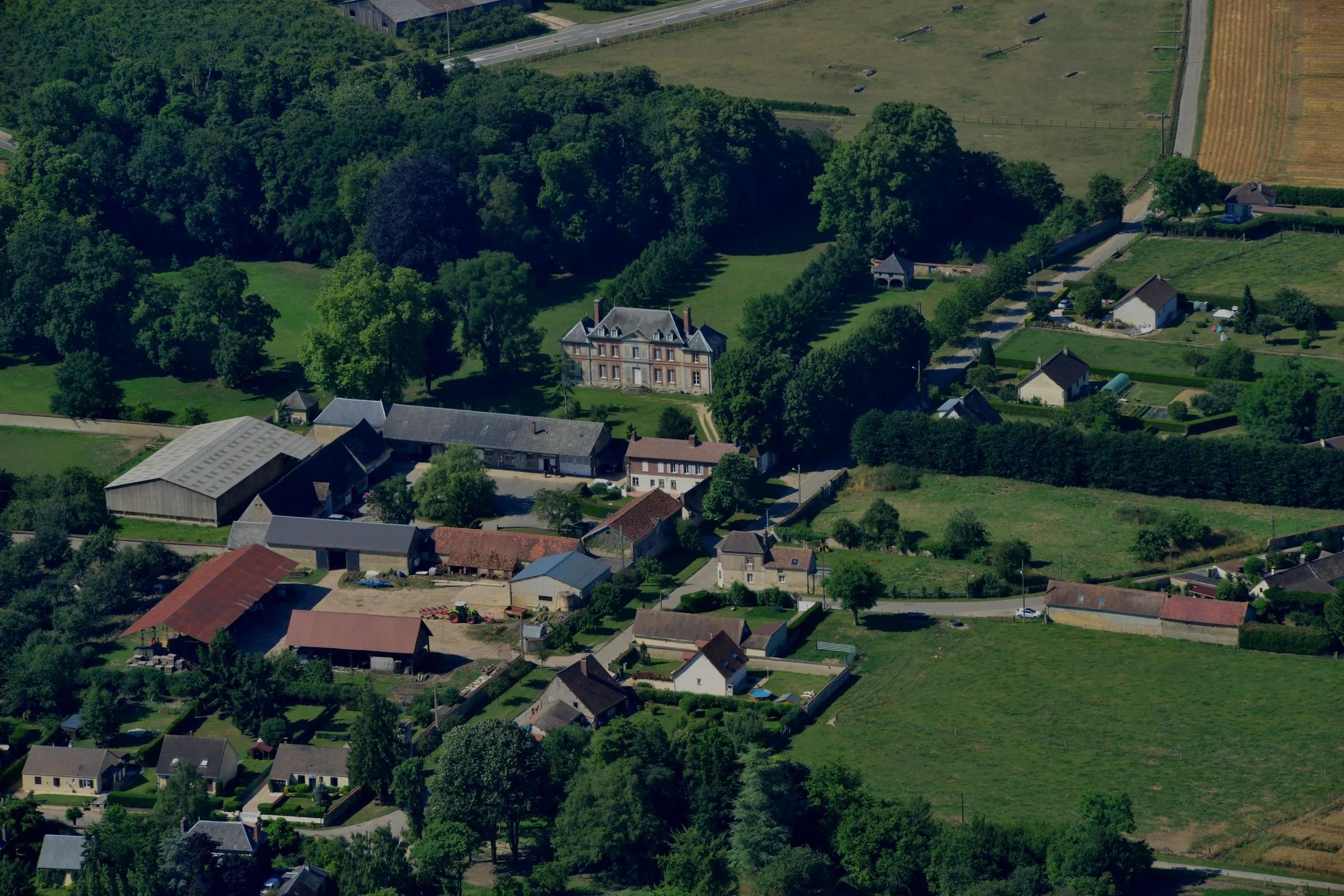 Aerial view of a countryside estate with a mansion, farm buildings, and surrounding greenery.