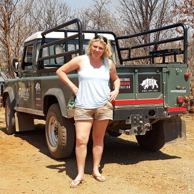 Woman standing next to a safari jeep in a dry, wooded area.
