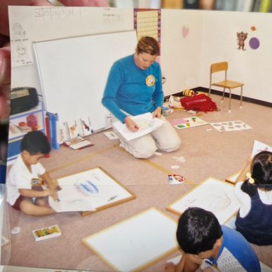 Teacher and children drawing together on the floor in a classroom.