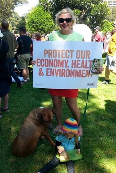 Woman holds a sign advocating for economy, health, and environment protection at an outdoor event.