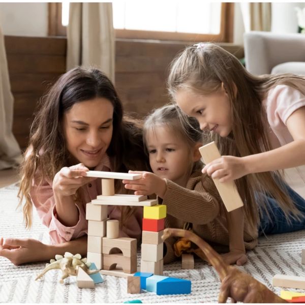 Mother and daughters building a tower with wooden blocks on the floor.