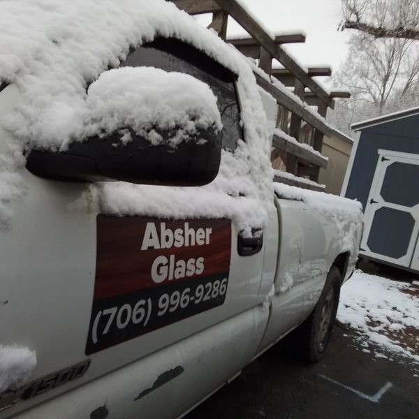 Snow-covered white truck with Absher Glass advertisement parked outside.