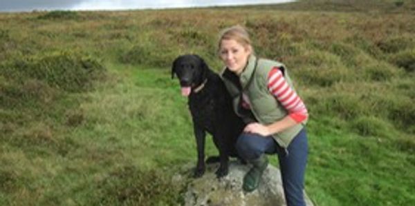 Woman posing with her black dog in a grassy field.