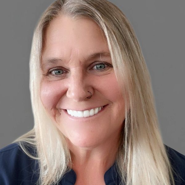 Smiling woman with blonde hair and blue eyes against a gray background.