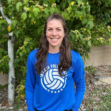 Smiling woman in a blue volleyball shirt outdoors with green foliage background.