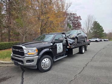 Tow truck carrying a damaged car with front-end collision on a cloudy day.