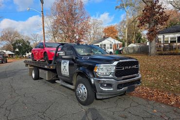 Black RAM tow truck carrying a red car on a residential street.