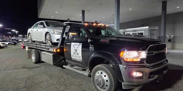 Black RAM tow truck carrying a silver sedan at night.