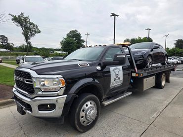 Black tow truck carrying a black car on a cloudy day.
