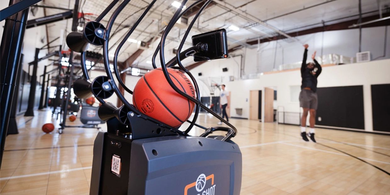 Basketball shooting machine with a player taking a shot in a gym.