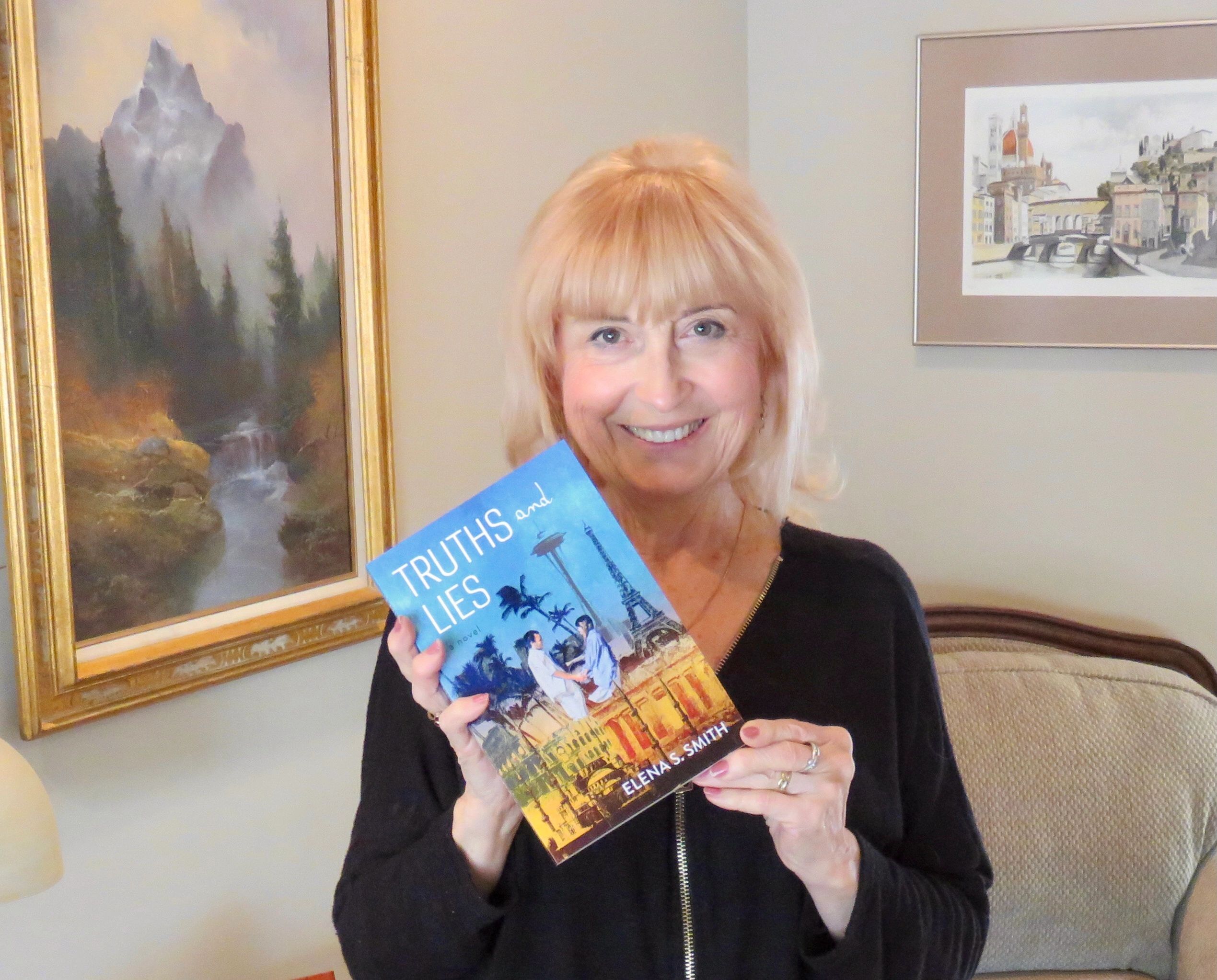 A woman smiling and holding a book titled "Truths and Lies" by Elena S. Smith.