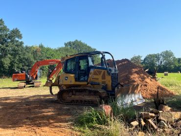 Construction site with a bulldozer and an excavator near a dirt pile.