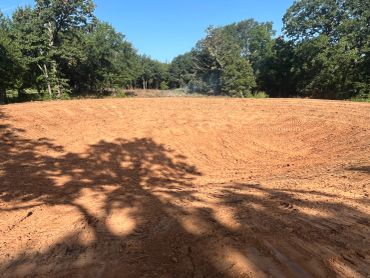 A freshly cleared dirt area surrounded by trees under a clear blue sky.