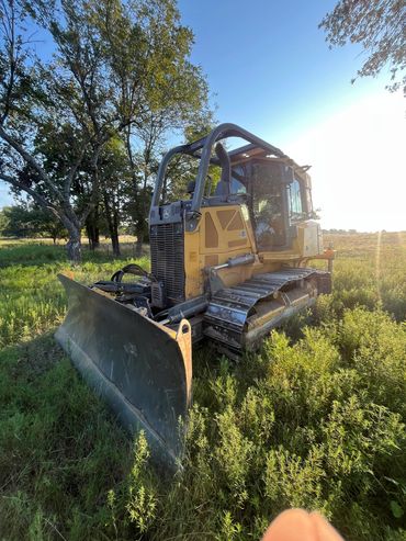 Yellow bulldozer parked in a grassy field under clear blue sky.