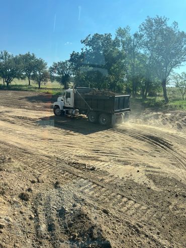 Dump truck unloading dirt at a construction site on a sunny day.