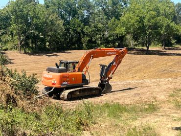Orange Hitachi excavator clearing land near trees.