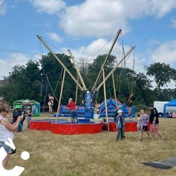 Children enjoying a bungee trampoline at an outdoor fair on a sunny day.