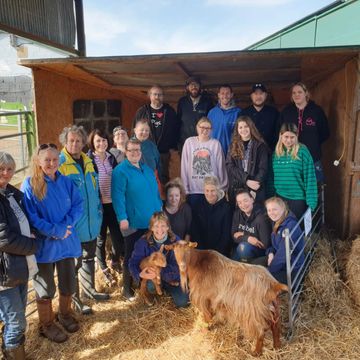 Group of people posing with a goat inside a barn on a sunny day.