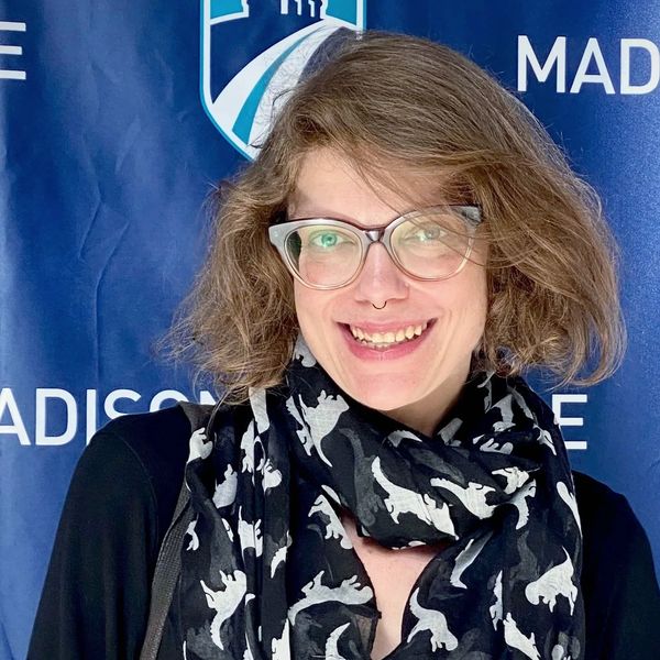 smiling woman with glasses wearing a dinosaur scarf