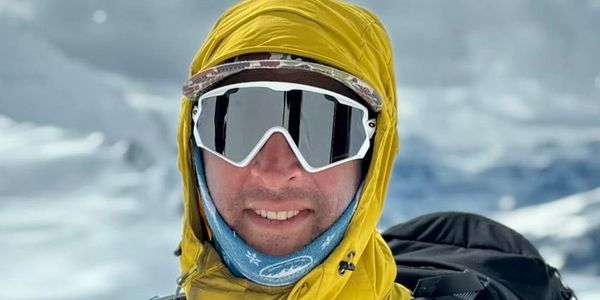 Person wearing reflective ski goggles and yellow hooded jacket in snowy environment.
