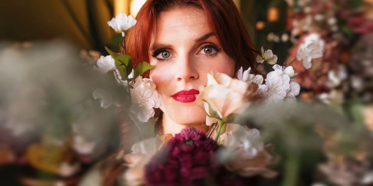 Woman with red hair surrounded by white and purple flowers.