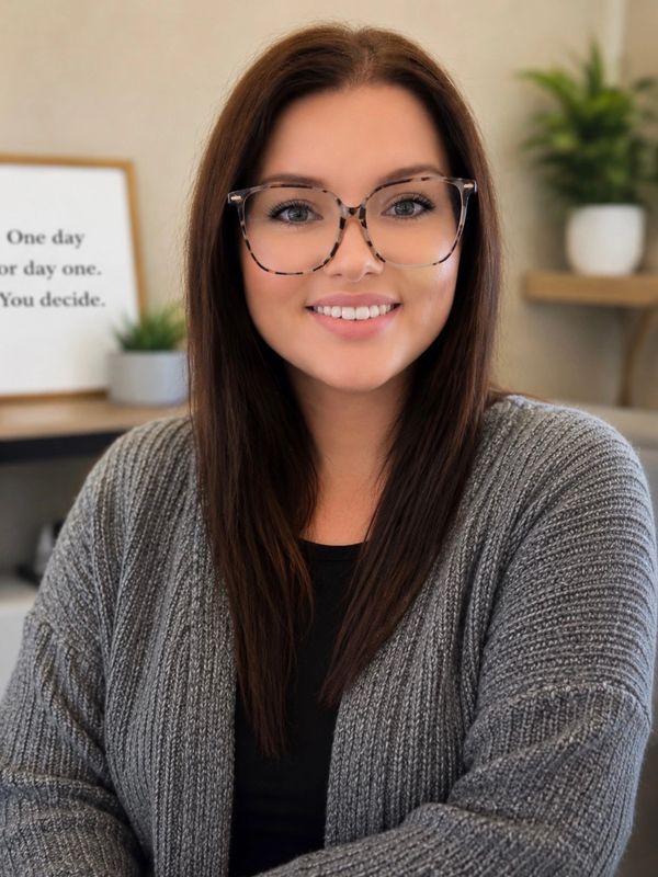 Smiling woman with glasses and long brown hair in cozy gray sweater.