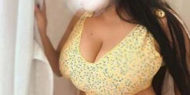 Woman in a yellow top and pink skirt posing near a curtain.