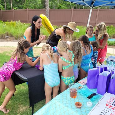 Children in swimsuits gathered around a table outdoors with adults supervising.