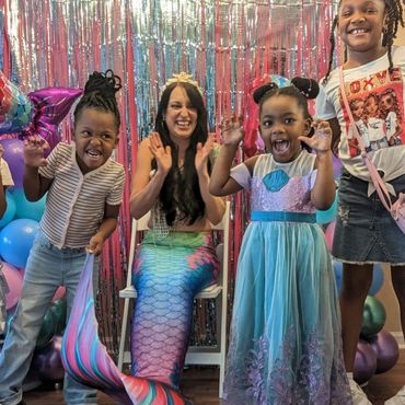 Children and a woman dressed as a mermaid having fun at a colorful party.