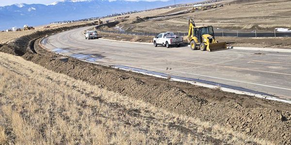 Newly paved road under construction with construction vehicles and mountainous backdrop.