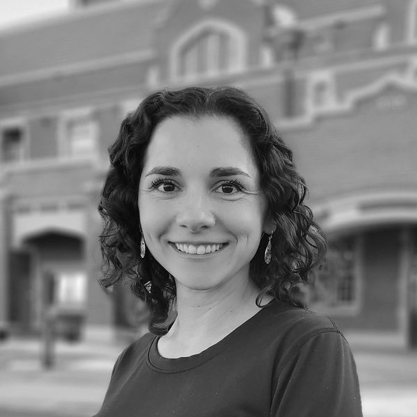 Smiling woman with curly hair in front of a blurred urban background.
