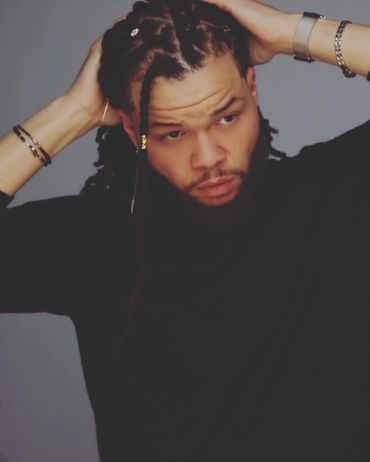 Man with braided hair adjusting his hairstyle, wearing bracelets and a watch.