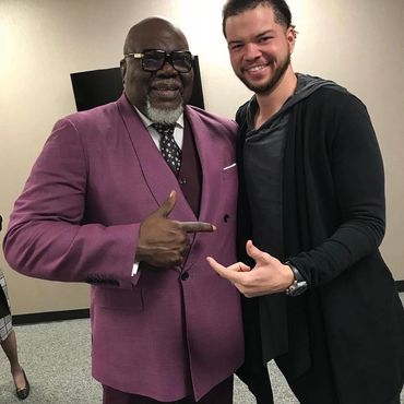 Two men smiling and pointing at each other in a casual indoor setting.