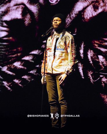 A man passionately sings on stage with artistic visuals behind him.