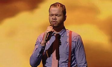 Man singing passionately on stage with eyes closed and microphone in hand.
