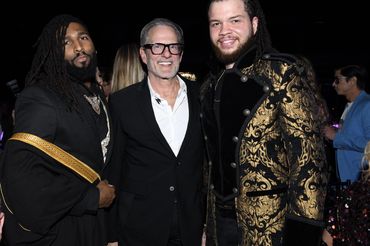 Three men posing at a stylish event, wearing elegant and bold outfits.